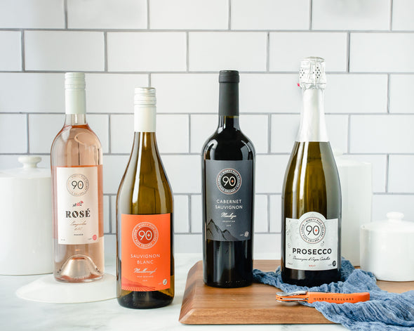 A bottle of Lot 33 Rosé from Languedoc, France, a bottle of Lot 166 Sauvignon Blanc from California, a bottle of Lot 53 Cabernet Sauvignon from Medoza, Argentina, and a bottle of Lot 50 Prosecco next to each other on a marble countertop with white back splash.