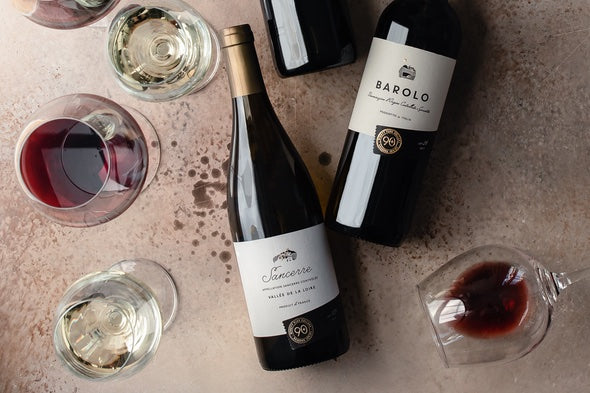 A bottle of Lot 126 Sancerre from Loire Valley, France and Lot 26 Barolo from Piedmont, Italy on a counter next to full glasses of wine.