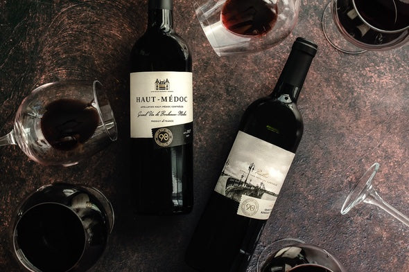 A bottle of Lot 202 Haut-Médoc and Lot 201 Pauillac Grand Vin De Bordeaux- Médoc on a counter next to full wine glasses.
